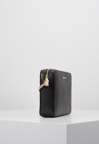 Sort lædertaske med tekstureret overflade. Guld lynlås og hardware. Firkantet form, kompakt design med en diskret brandlogo på forsiden.