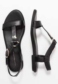 Svarta lädersandaler med en minimalistisk design, justerbara remmar, rund tå och en platt sula med en subtil metallisk accent.