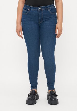 Skinny blue denim jeans with a high waist, featuring subtle stitching and five-pocket design. Paired with chunky black platform shoes.