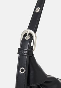 Cinghia di una borsa in pelle nera con una fibbia in metallo argento, caratterizzata da una texture liscia e piccoli occhielli argentati per ulteriori dettagli.