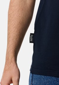 Mørkeblå bomulds t-shirt med et side-mærke. Korte ærmer, tætsiddende pasform og glat tekstur synlig på stoffet.