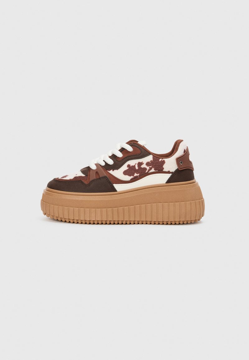 Platform sneakers with a brown and cream camouflage pattern, contrasting tan soles, and white laces. The upper features mixed materials and textures.