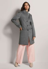 Grijze wollen jas met een gekleed kraag, drie knopen en zijzakken, gecombineerd met roze wijde broek en beige hakken. Een gladde textuur.