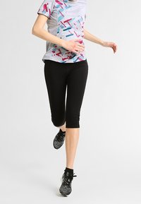 Helles graues Sportshirt mit einem bunten geometrischen Muster, kombiniert mit schwarzen Capri-Leggings und schwarzen Laufschuhen.
