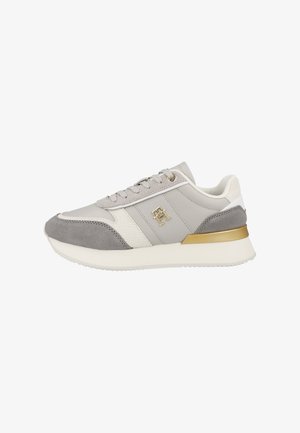 Zapatilla de deporte gris claro con paneles de ante y cuero liso, detalles en blanco y herrajes dorados. Cuenta con una suela texturizada y un diseño de cordones.