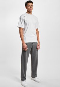 Hvid kortærmet t-shirt parret med grå sweatpants. Bukserne har sidesømme og er dækket af en snor. Hvide sneakers fuldender looket.