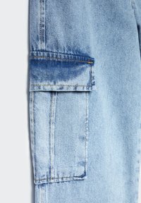 Pantalones cargo de denim azul claro con un gran bolsillo lateral, detalles de costura y una textura ligeramente desvanecida para un aspecto desgastado.