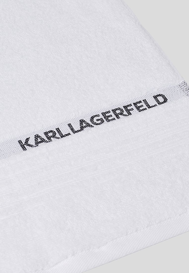 Biała bawełniana ręcznik o fakturowanej powierzchni, z gładkim białym brzegiem i czarnym logo "KARL LAGERFELD" na krawędzi.