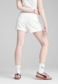 Shorts atletici bianchi con elastico in vita, abbinati a scarpe da ginnastica rosa e bordeaux e calze bianche con logo. Texture del tessuto liscia.