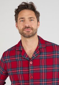 Camicia da pigiama a scacchi rossi in tessuto flanella, con colletto, chiusura a bottoni e linee blu e bianche a contrasto nel motivo.