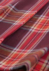 Tessuto tartan rosso e viola con strisce orizzontali e verticali, caratterizzato da accenti blu, verdi e arancioni. Texture morbida con un design tessuto.