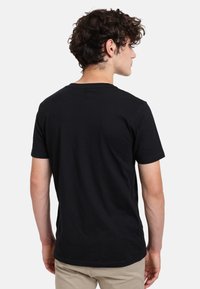 Svart kortärmad t-shirt i bomull med rund halsringning, avslappnad passform och slät yta, visas bakifrån.