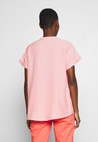 Camiseta de manga corta a rayas rosas con un ajuste relajado y escote redondo, combinada con pantalones de color melocotón. Textura suave, diseño casual.