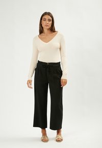 Top a maniche lunghe, con scollatura a V in morbido tessuto beige; pantaloni neri a gamba larga con vita legata e dettaglio dei bottoni; design minimalista.