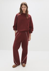 Bordeaux sweatshirt met ballonmouwen en witte piping, gecombineerd met bijpassende wijde broek met witte accenten en zijzakken.