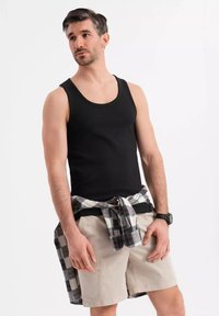 Svart ribbad linne i kombination med beiga shorts. En rutig skjorta knuten i midjan har svarta, vita och röda mönster. Svart klocka på handleden.
