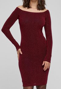 Robe bordeaux à épaules dénudées avec des manches longues, silhouette cintrée, et tissu texturé scintillant, atteignant le milieu de la cuisse.