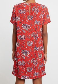 Röd kortärmad klänning med blommönster i lila och vitt. Har en nyckelhålöppning på baksidan och en avslappnad passform.