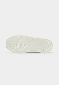 Semelle de basket blanche avec des motifs à chevrons et à rayures, détail de ligne diagonale et marquage Tommy Hilfiger au centre.