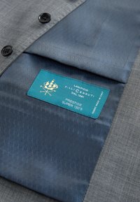 Fodera del completo a motivo blu con etichetta turchese con la scritta "Lanificio F.lli Cerruti Dal 1881 Prestige Super 130's Fabric Made in Italy."