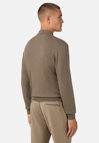 Pruun kootud pullover kaelusega, millel on sile tekstuur ja soonikkud. Kandmiseks heledate beežide pükstega, millel on lukuga tasku.