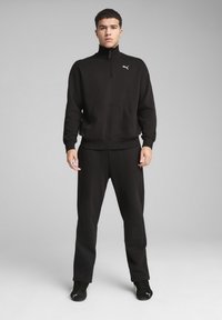 Sort hættetrøje med lynlås og høj krave, kængurulomme og Puma-logo. Sammen med matchende sorte sweatpants og sorte sneakers.