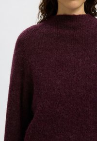 Pull en tricot bordeaux avec un col montant, présentant une texture douce et pelucheuse et une coupe décontractée, mettant en valeur une couleur riche et profonde.