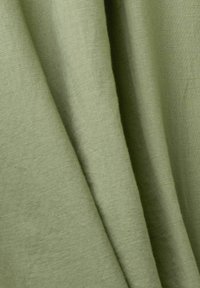 Tessuto di lino verde con una superficie liscia, caratterizzato da dolci drappeggi e pieghe sottili, che mostrano un aspetto naturale e organico.