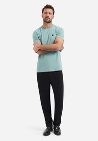 Licht mintgroene t-shirt met korte mouwen en een ronde hals, gecombineerd met zwarte broek en zwarte schoenen, met een klein logo op de borst.