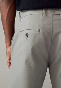 Pantalon pour homme gris clair avec une surface texturée, présentant une poche arrière avec un bouton foncé et une coupe slim.