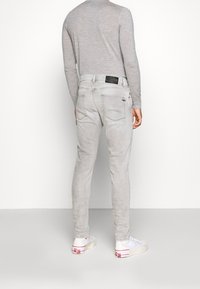 Jeans de mezclilla gris con un corte ajustado, que presentan bolsillos traseros, una parche de cuero negro, y combinados con zapatillas blancas. Textura suave, con mínimas embellishments.