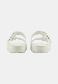 Sandalias blancas con un acabado suave, que presentan una amplia correa con acento de lazo, abertura en la parte trasera y suela texturizada. Diseño simple y minimalista.