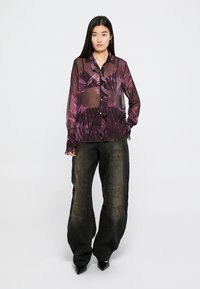 Blusa roxa transparente com estampa tropical, com botões e mangas compridas. Combinada com calças largas escuras e texturizadas e sapatos pontiagudos.