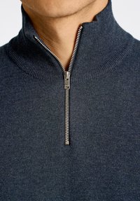 Tummansininen vetoketjullinen neulepusero, joka on valmistettu pehmeästä neulekankaasta. Varusteena ribbed-kaulus ja metallivetoketju.