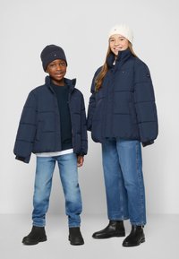 Marina puffjackor med höga kragar, ribbstickade mössor (en marina, en krämfärgad), tillsammans med ljusblå jeans och svarta anklar stövlar.