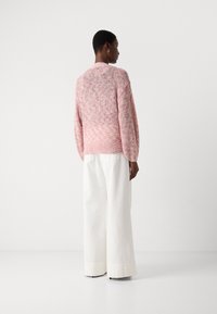 Maglione rosa lavorato a maglia con un design a trama e maniche lunghe, abbinato a pantaloni bianchi a gamba larga con vita alta. Materiali morbidi e leggeri.