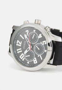 Orologio cronografo con quadrante nero, dettagli argentati e grandi numeri bianchi. Presenta tre sottomisure e un cinturino in silicone nero.