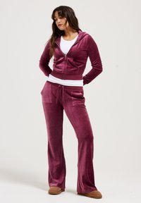 Velvet tracksuit in dark berry color featuring a zip-up cropped hoodie and flared pants with two front pockets and an elastic waistband.
