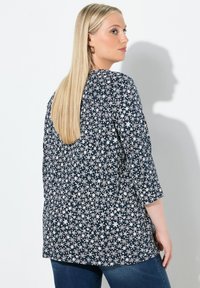 Marineblaue Tunika mit einem weißen Blumenmuster, Dreiviertelärmel und lockerem Schnitt. Hergestellt aus weichem Stoff, geeignet für Freizeitmode.