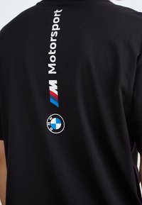 Mustat t-paidat, joissa on valkoinen "Motorsport" -teksti ja BMW-logot punaisena, sinisenä ja valkoisena takana. Pehmeää puuvillamateriaalia, jossa on pyöreä kaula-aukko.