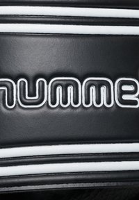 Matériau synthétique noir avec des accents rayés blancs ; présente un texte stylisé en relief "humme" dans une police audacieuse et moderne.