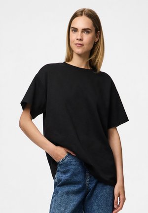 T-shirt noir oversize en coton avec des manches courtes, un col rond et une coupe ample, associé à un jean en denim bleu clair.