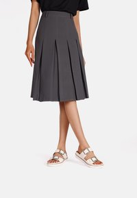 Gonna grigia a pieghe con cintura aderente, abbinata a sandali beige chiaro con doppie cinghie e dettagli metallici.