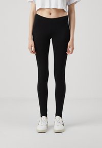 Black leggings in a fitted design, made from a stretchy material, featuring a smooth texture. Worn with white sneakers.