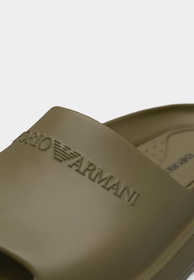 Κοντινή λήψη πράσινου χακί σαγιονάρας με ανάγλυφο λογότυπο Emporio Armani στο λουράκι.