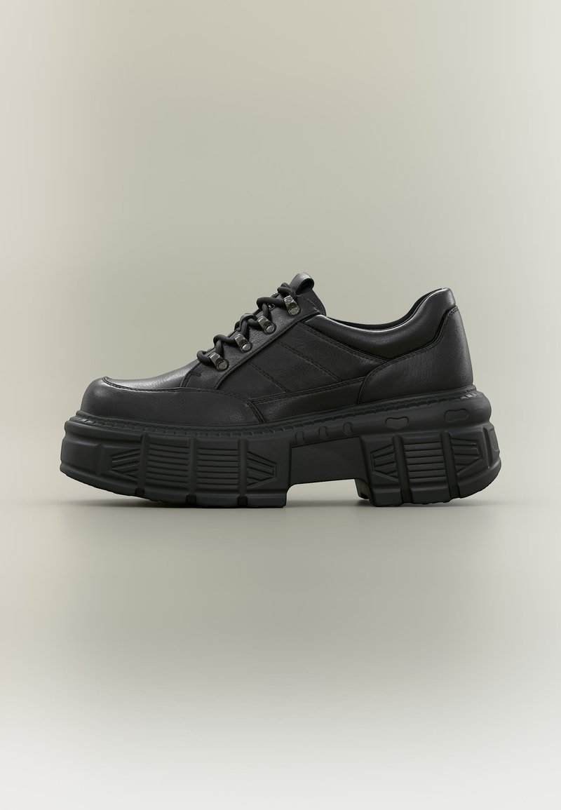 Μαύρο platform αθλητικό παπούτσι από δέρμα με χοντρή υφή στη σόλα, κορδόνια μπροστά και επένδυση στον αστράγαλο, σε ουδέτερο φόντο.