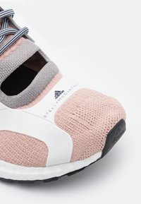 Baskets tricotées rose clair avec des accents gris, semelle intermédiaire blanche et semelle extérieure noire. Comprend des détails de logo et des lacets rayés.