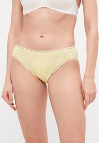 Gule bomullstruser med blondekantdetaljer langs midjebåndet og benåpningene. Har en logo på forsiden.