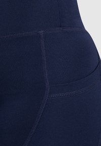 Leggings de sport bleu marine avec une texture lisse, dotés de coutures plates et d'une poche latérale pour le rangement. Des surpiqûres accentuent la durabilité.