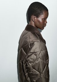 Bruine geborduurde jas met een ruitpatroon, voorzien van een corduroy kraag. De stof heeft een gladde textuur en het ontwerp is oversized.